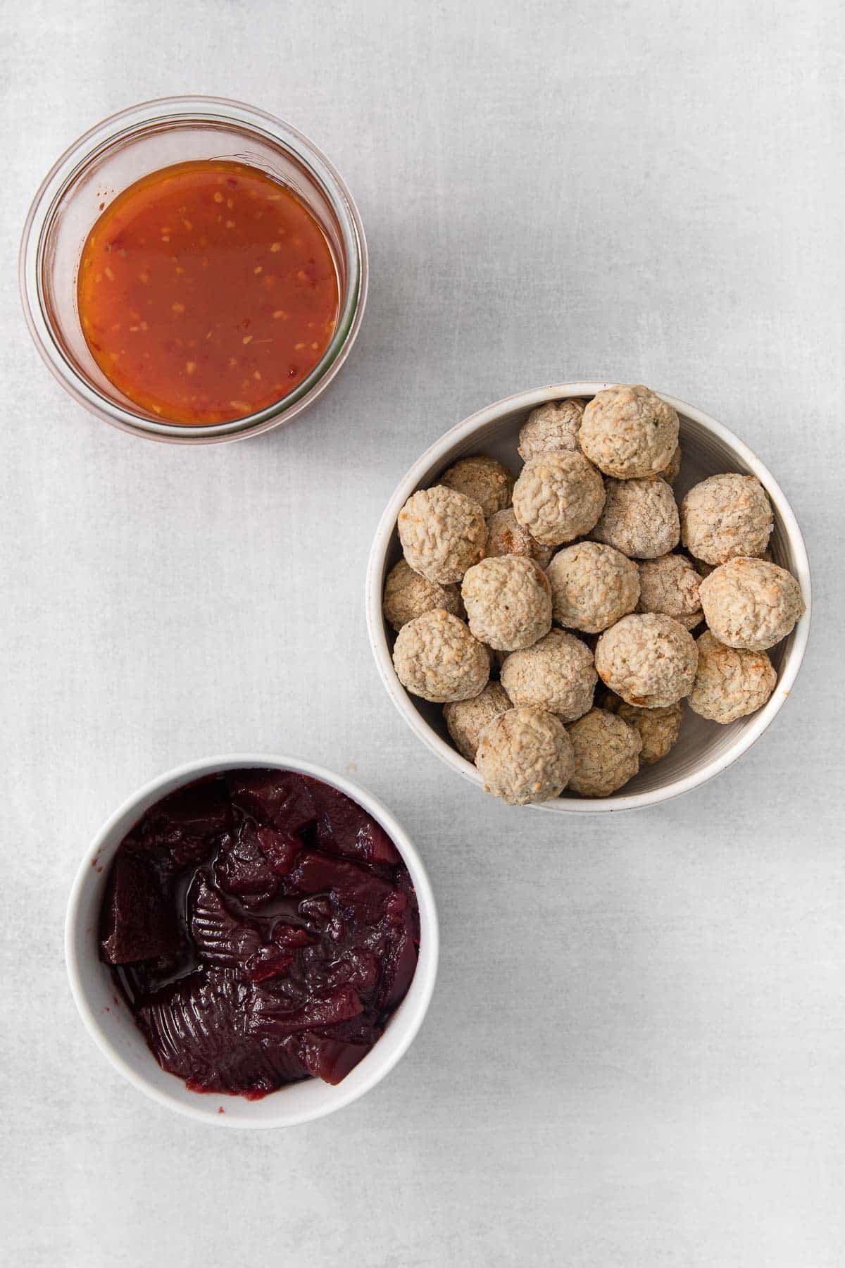 three white bowls. one with frozen meatballs, one with jellied cranberry sauce and one with sweet chili sauce.