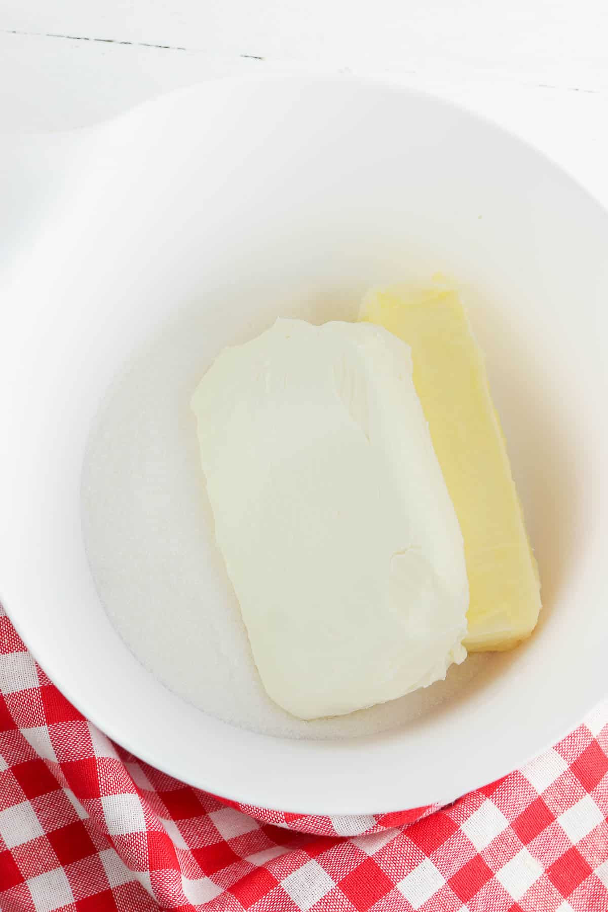 white mixing bowl with cream cheese, butter and white sugar.