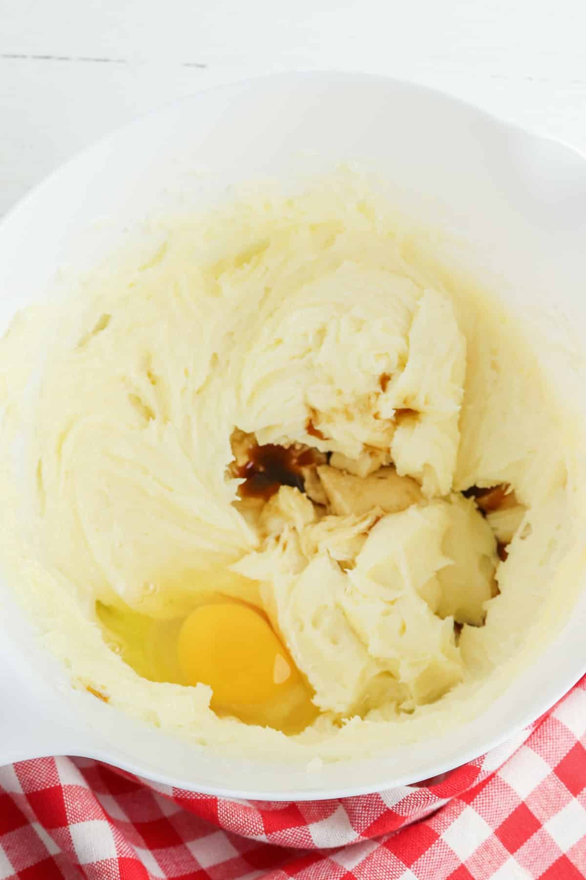 white mixing bowl with creamed butter with a raw egg and vanilla extract on top.