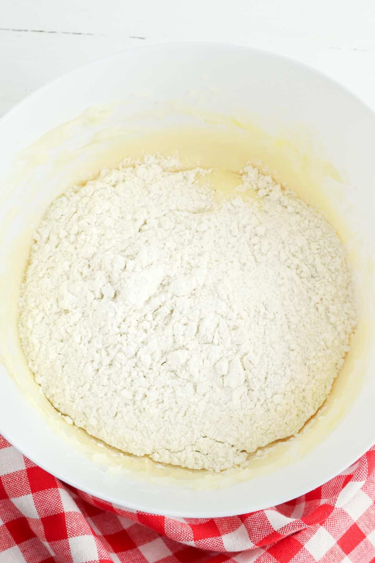 white mixing bowl with flour on top of fluffy butter mixture.