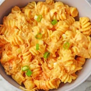 white bowl full of buffalo chicken mac and cheese topped with sliced green onions.