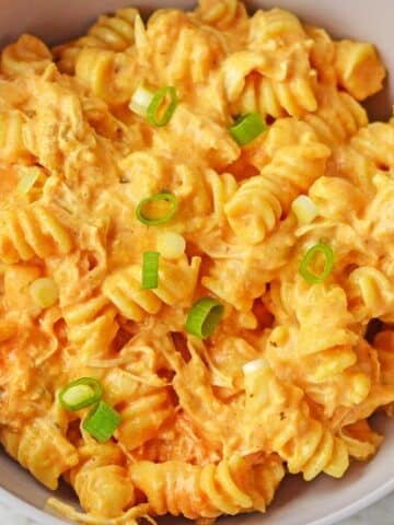 white bowl full of buffalo chicken mac and cheese topped with sliced green onions.