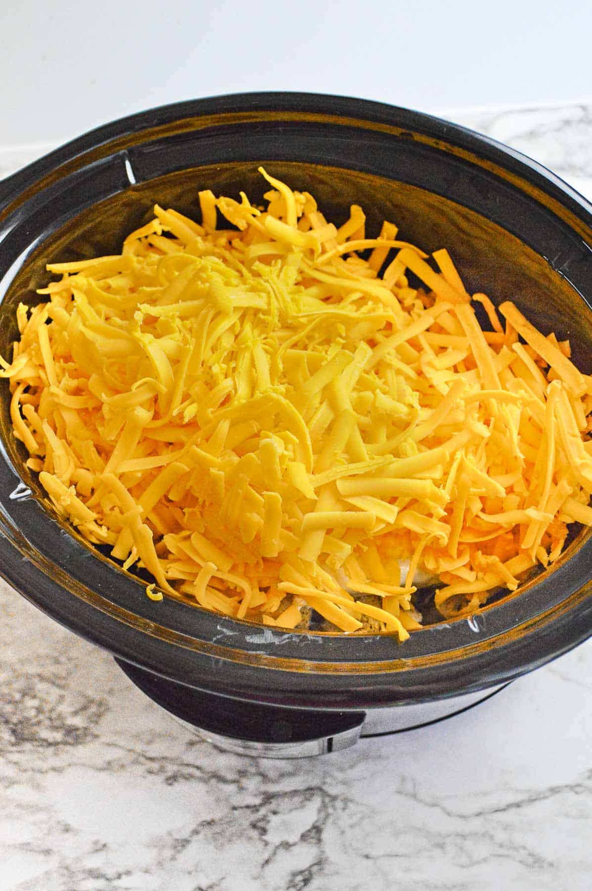 shredded cheese over chicken in a black slow cooker.