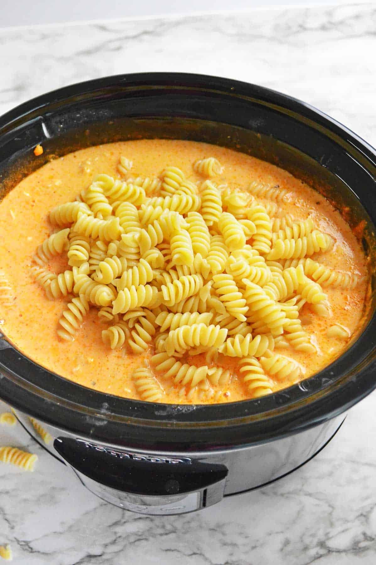 rotini noodles in a cheesy sauce in a crock pot.