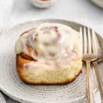 closeup of a cinnamon roll with icing on a plate with 2 forks.