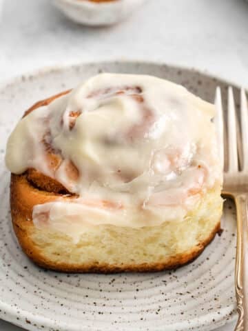 closeup of a cinnamon roll with icing on a plate with 2 forks.