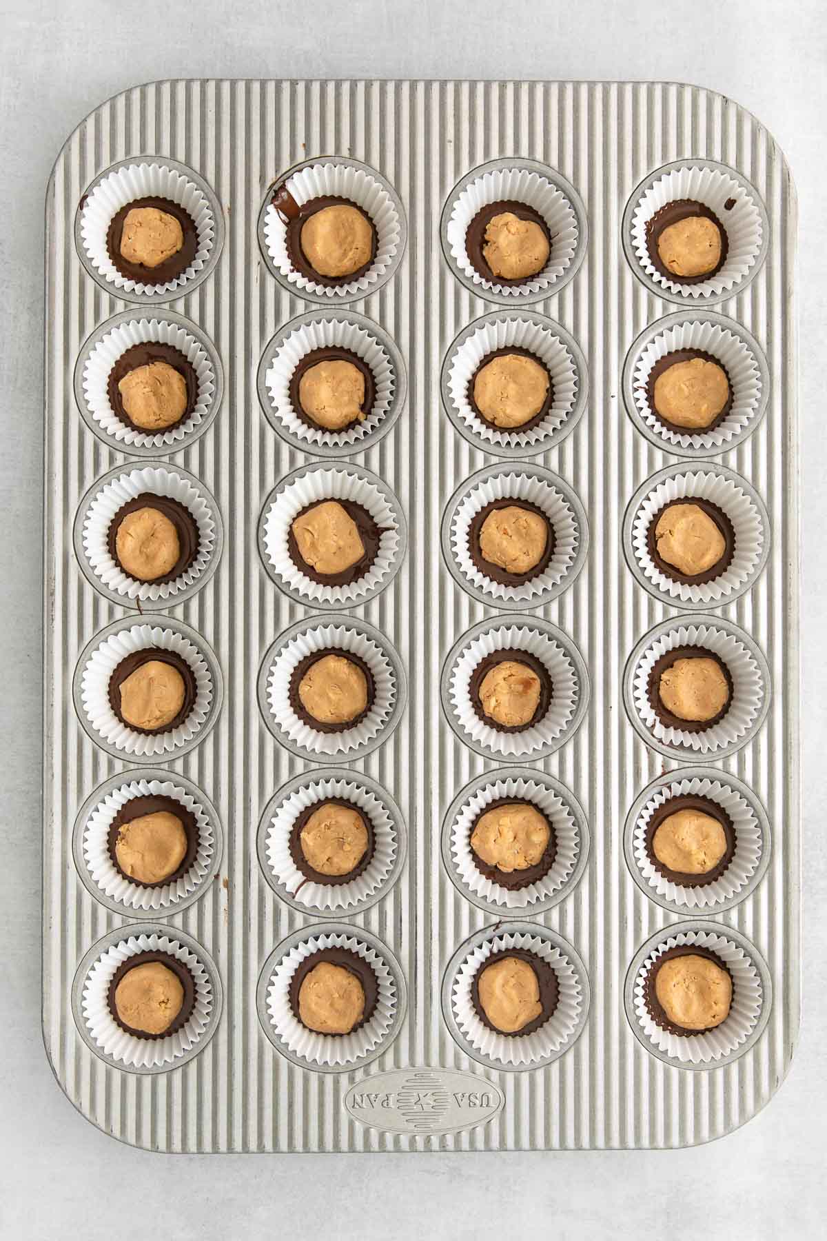 lined mini muffin tin with chocolate and peanut butter dollop on top.