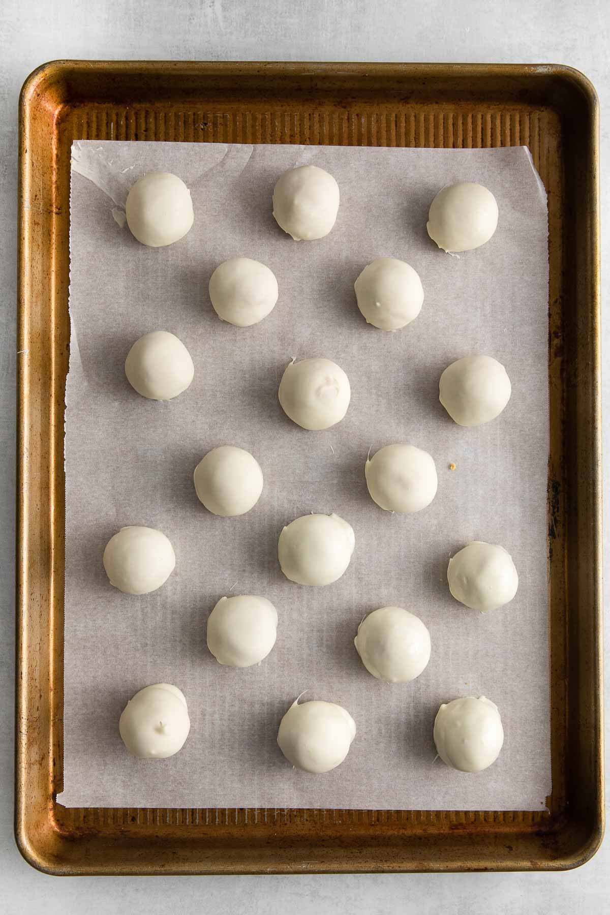 eighteen white chocolate covered peanut butter balls on a parchment paper lined cookie sheet.