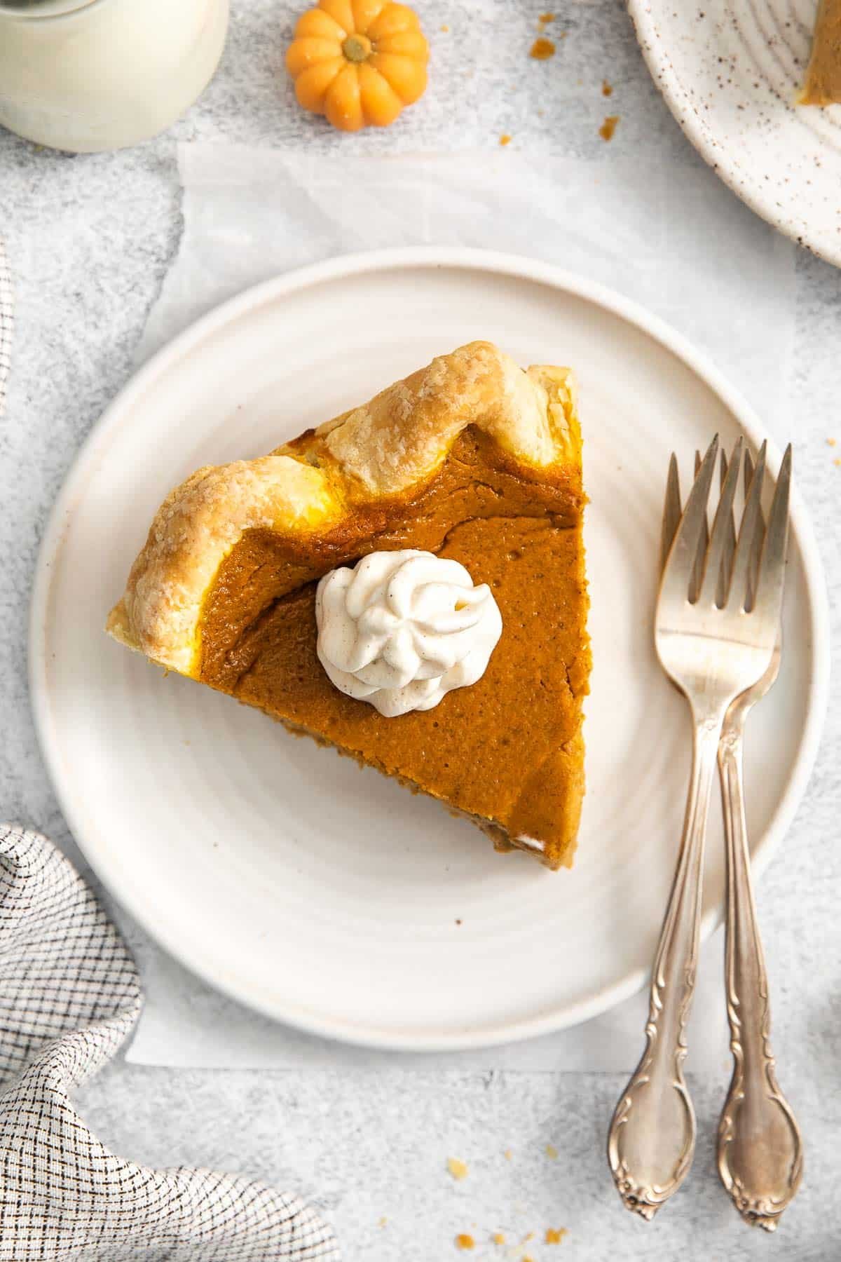 closeup of a slice of pumpkin pie topped with a dollop of whipped cream on a white plate with two forks on the plate.