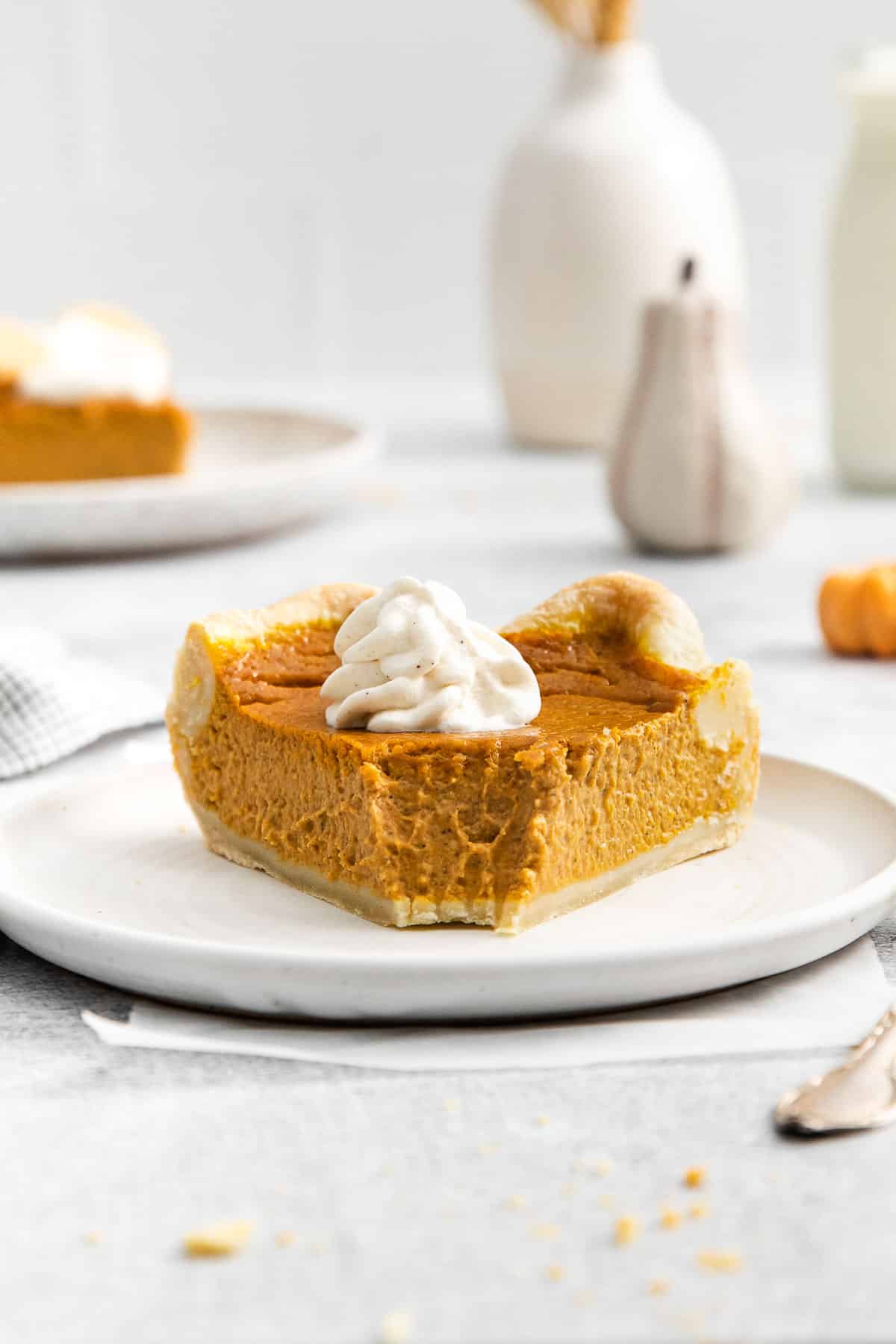 slice of pumpkin pie with a bite missing on a white plate.