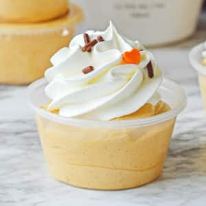 small plastic shot cup with pumpkin pie pudding shot with whipped cream on top.