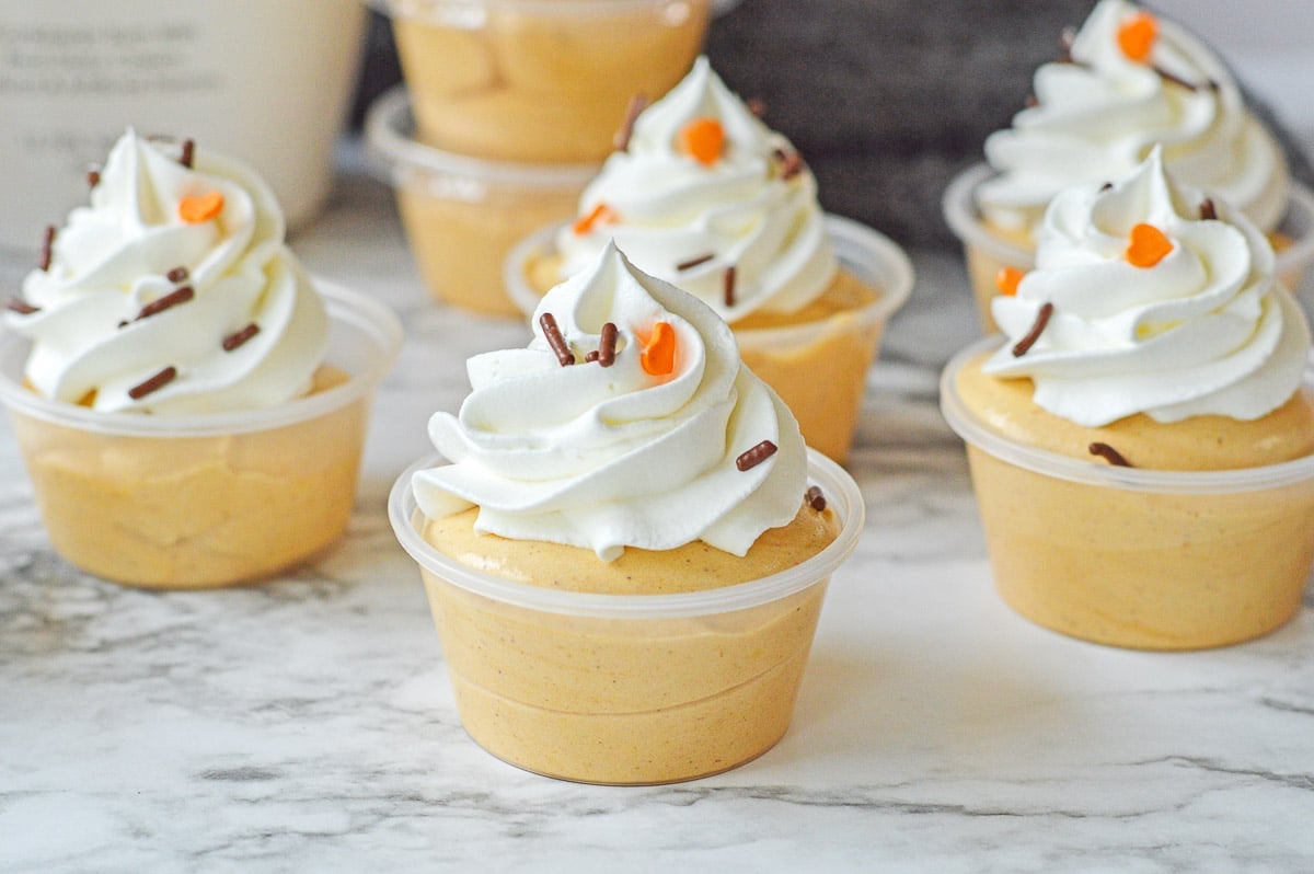 several small plastic shot cups filled with pumpkin pudding and topped with whipped cream.