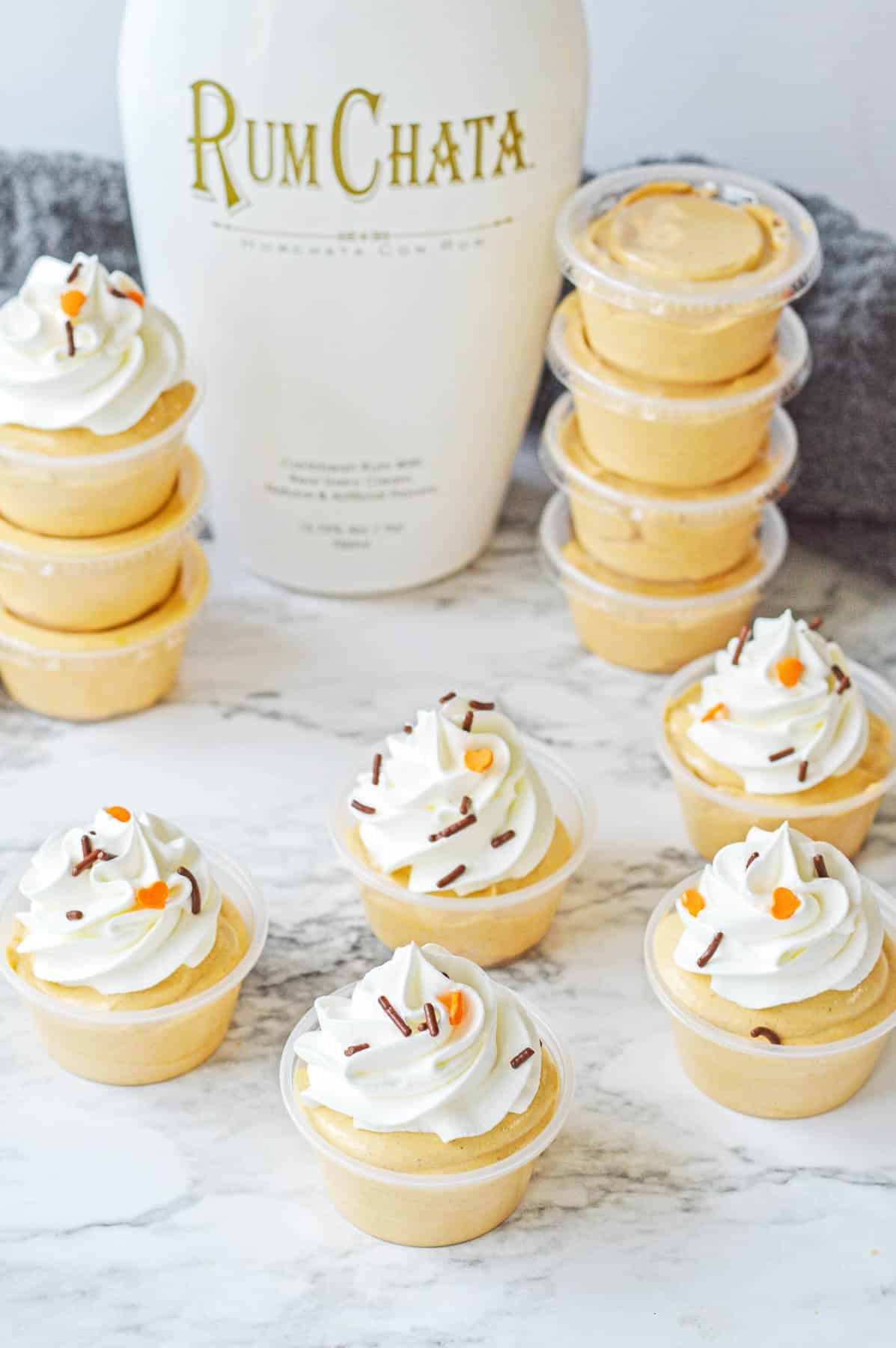 five pumpkin pudding shots topped with whipped cream and chocolate and orange sprinkles on a counter.