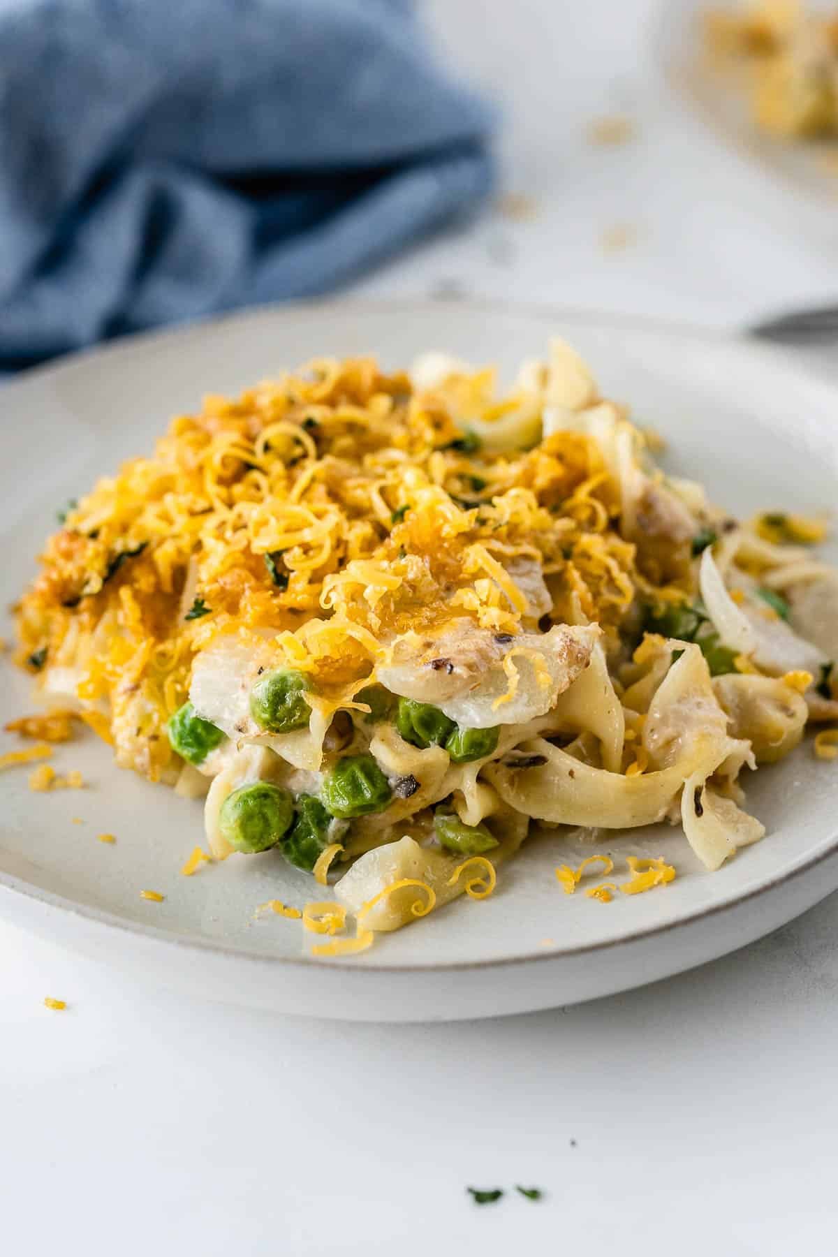 white plate with tuna casserole with egg noodles, peas and a crunchy topping.