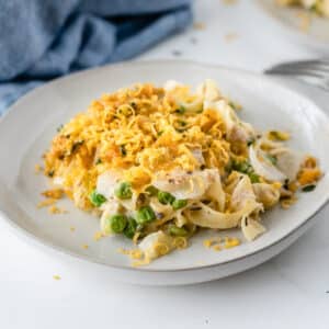 plate full of tuna casserole with egg noodles and peas topped with a crunchy cornflake topping and cheese.