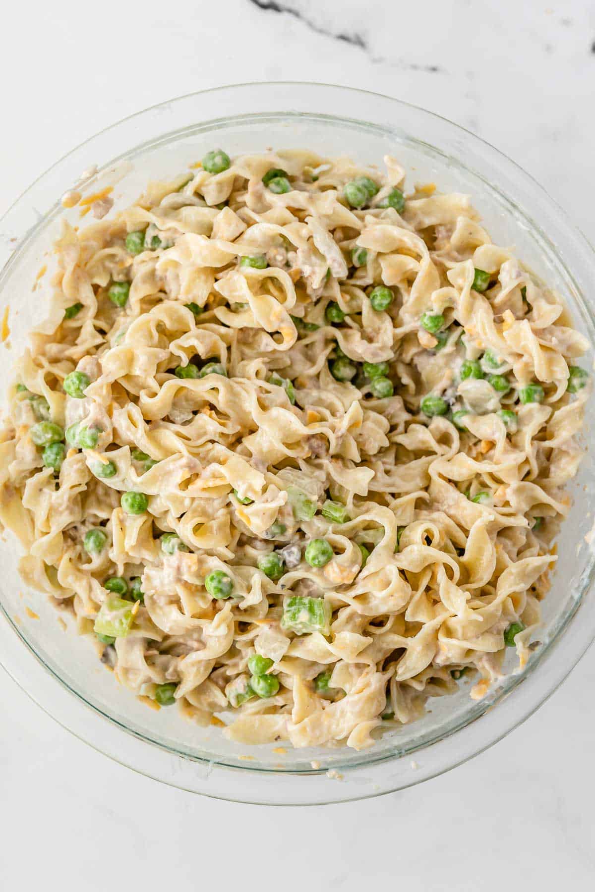 egg noodles mixed in creamy soup and peas mixture in a big glass bowl.