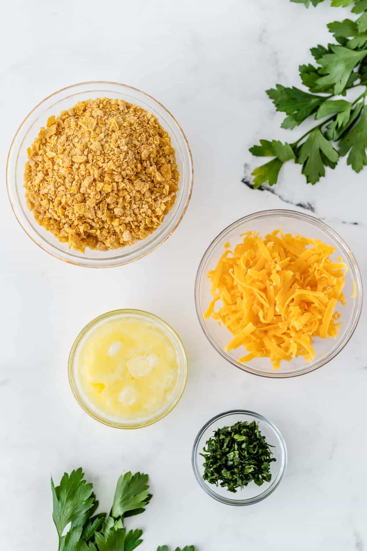 four glass bowls with crushed cornflakes, melted butter, shredded cheese and parsley.
