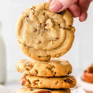 closeup of a butter pecan cookie held over a stack of cookies