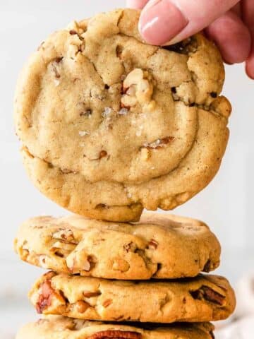closeup of a butter pecan cookie held over a stack of cookies
