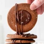 closeup of a chocolate thumbprint cookie being held with a woman's fingers over a stack of cookies