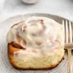 closeup of a homemade cinnamon rolls with icing on a white plate.