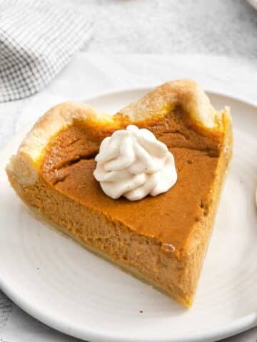 white plate with a slice of pumpkin pie with a dollop of whipped cream on top