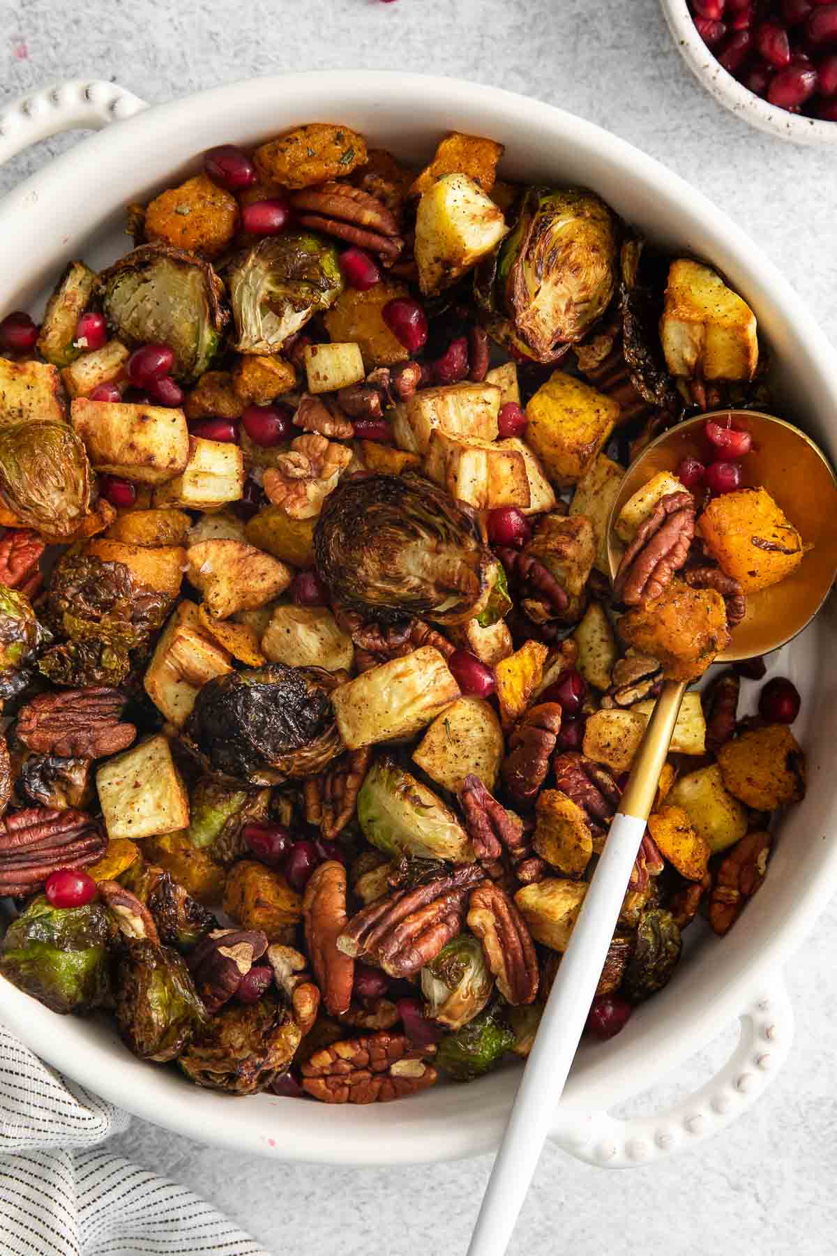 white serving bowl with air fryer vegetables with brussel sprouts, butternut squash, parsnips, pecans and pomegranate seeds.