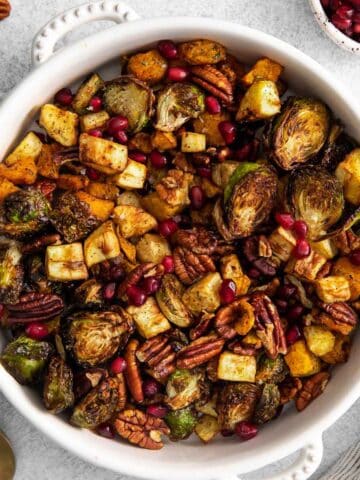 white serving bowl with air fried vegetables - brussel sprouts, butternut squash, parsnips, pecans and pomegranate seeds.