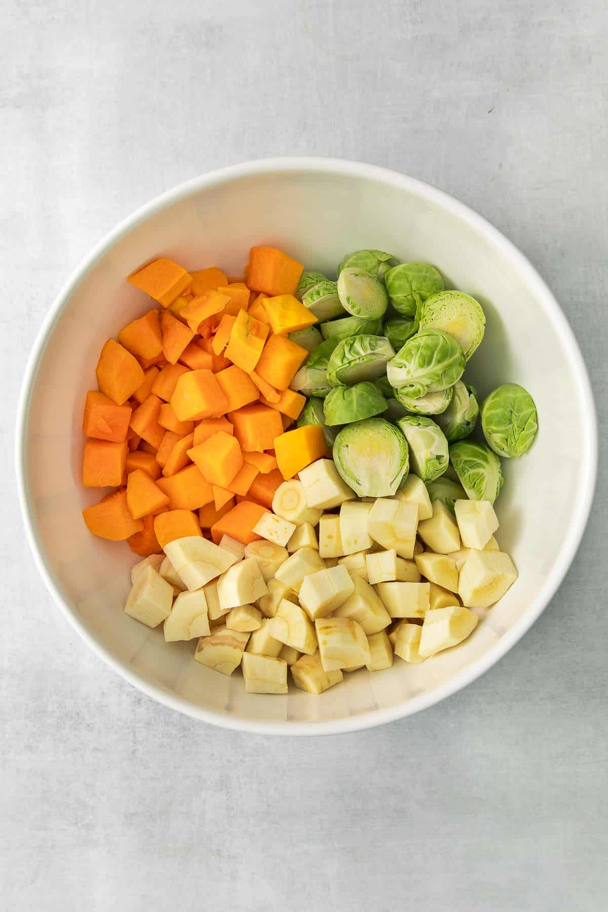 white bowl with sliced brussel sprouts, butternut squash and parsnips.