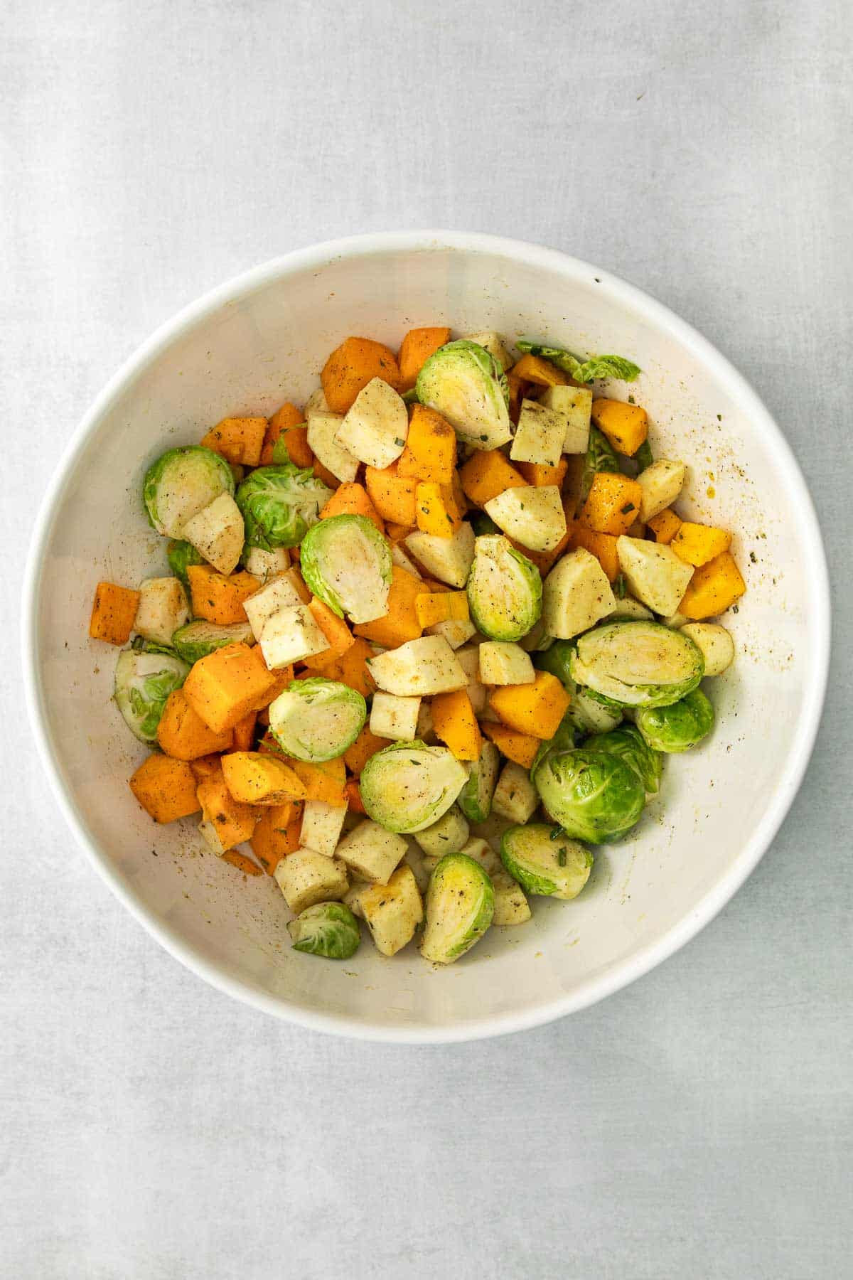 white bowl with brussel sprouts, parsnips and butternut squash cubed and tossed in oil and spices.