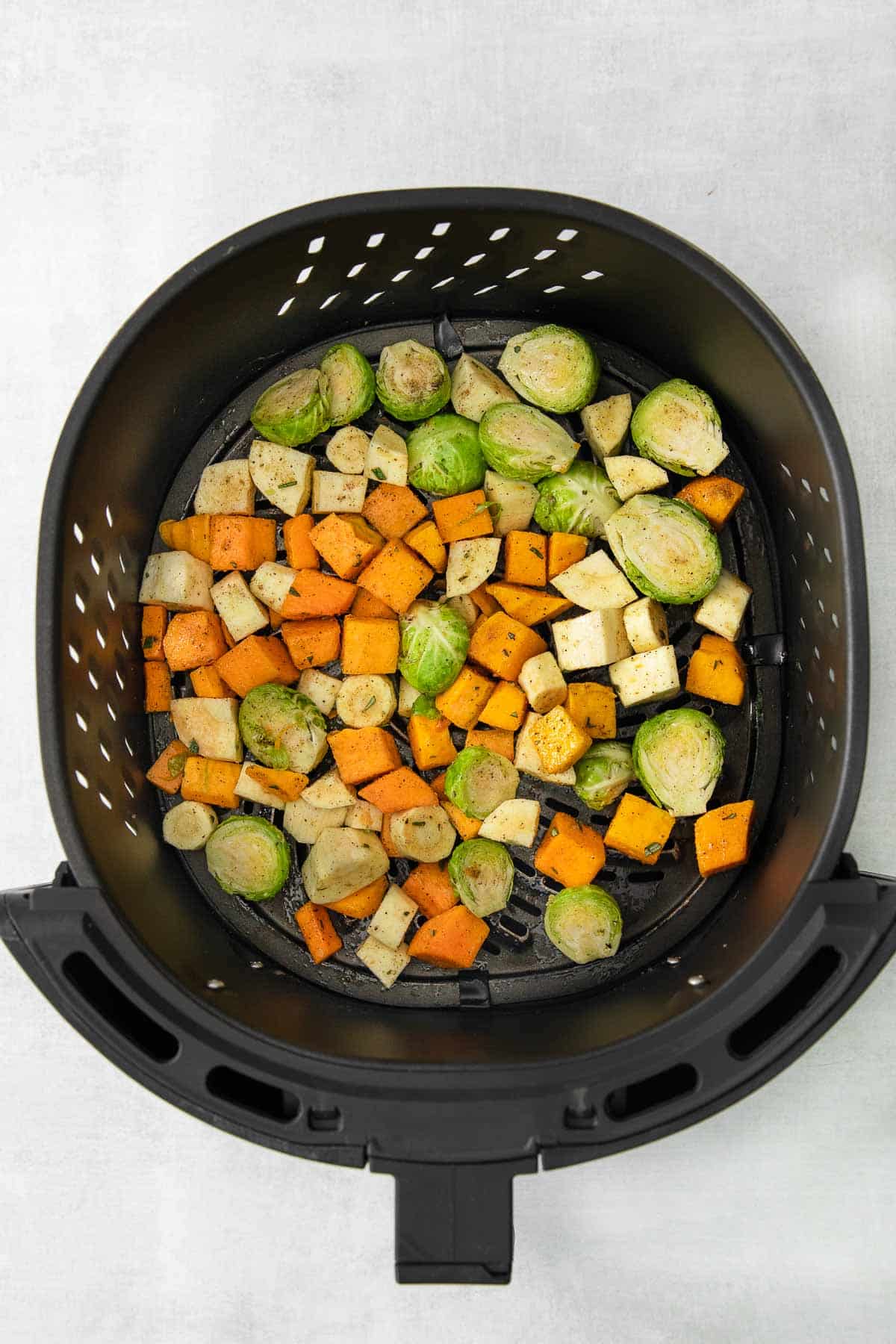 black air fryer basket with raw diced brussel sprouts, butternut squash and parsnips.