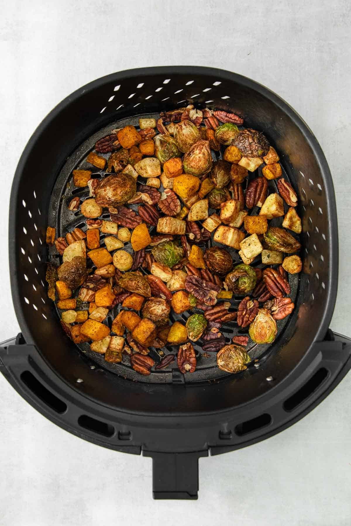 black air fryer basket with roasted brussel sprouts, butternut squash, parsnips and pecan halves.
