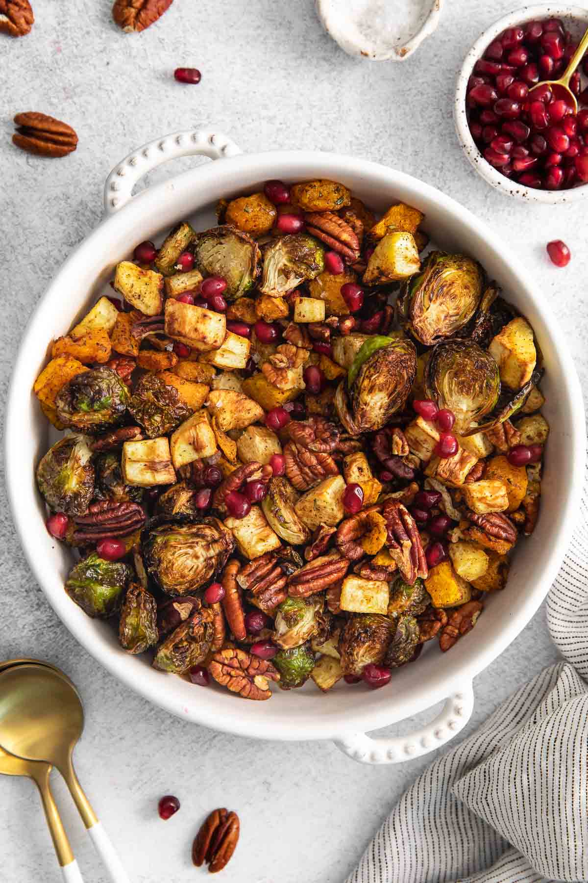 white serving bowl with air fryer roasted vegetables - brussel sprouts, butternut squash, parsnips, pecans and pomegranate seeds.
