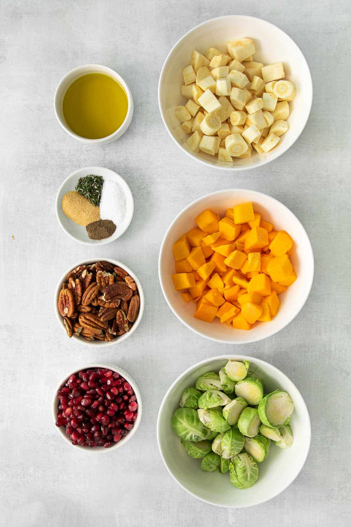 several white bowls with ingredients for air fryer vegetables - white serving bowl with air fryer roasted vegetables - sliced brussel sprouts, diced butternut squash and parsnips, pecan halves, pomegranate seeds, olive oil and spices.