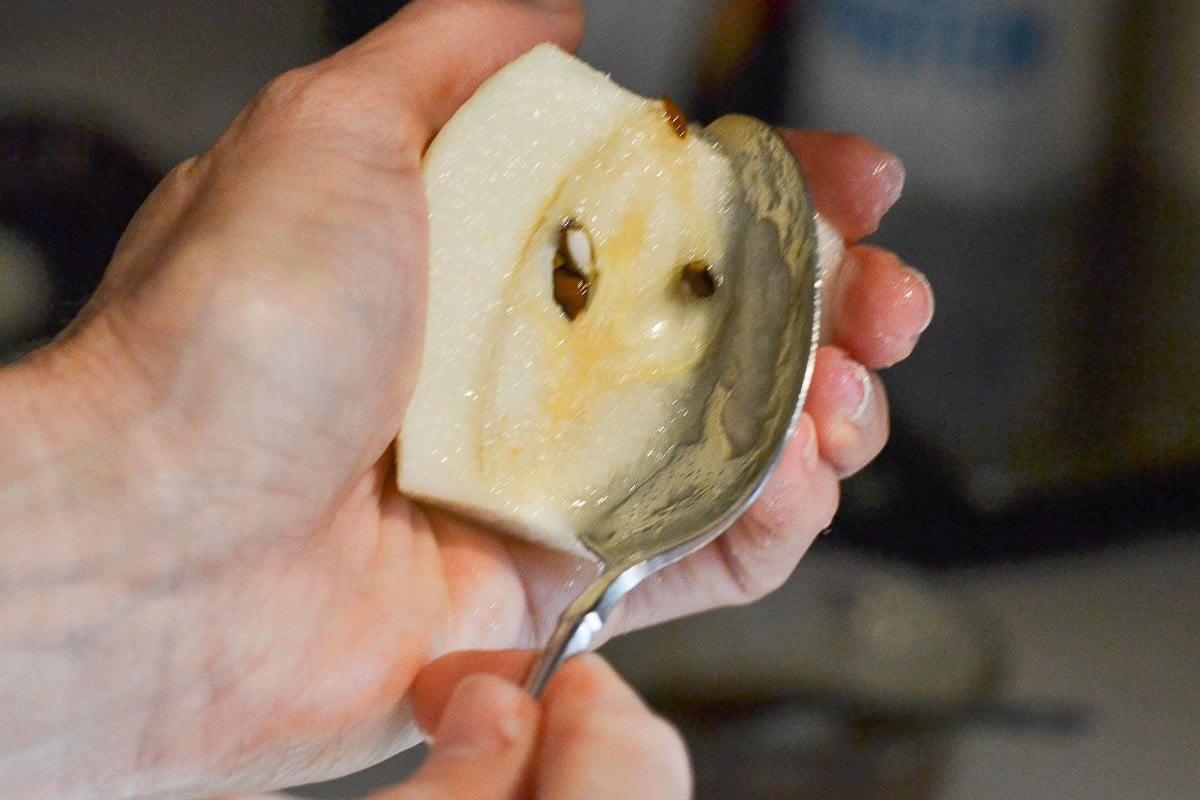 woman's hand holding a pear half and scooping the core out with a spoon.