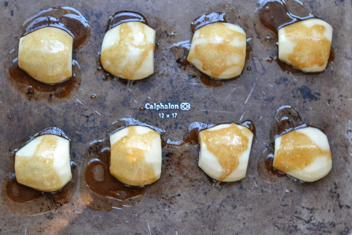 eight pear halves face down on a baking sheet with honey and cinnamon drizzled over top.
