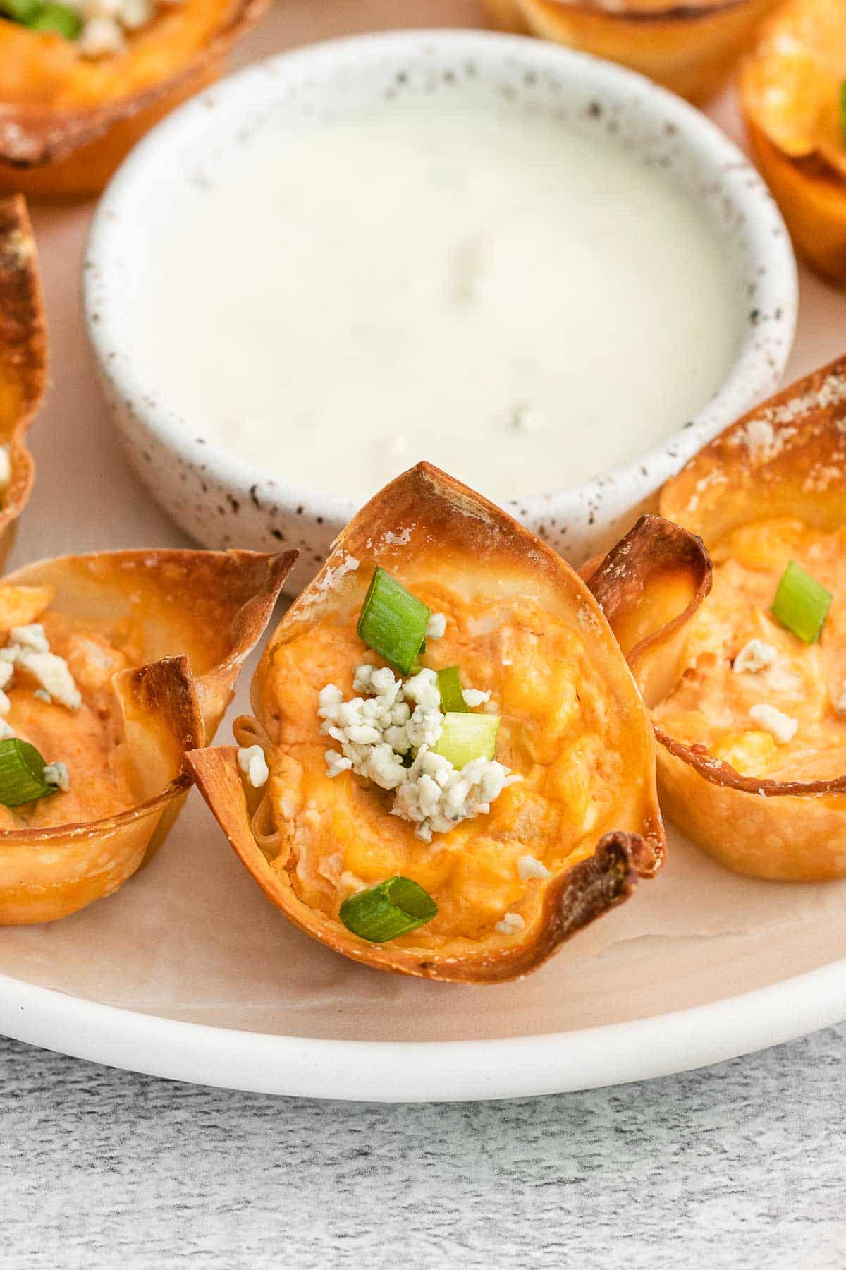 closeup of a buffalo chicken wonton with blue cheese and green onions on a white plate.