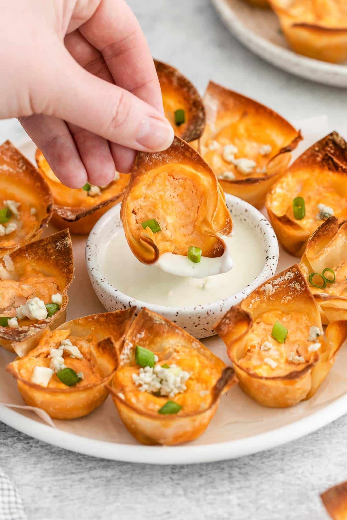 baked wonton wrapper filled with buffalo chicken and cheese filling being dipped into blue cheese dressing.