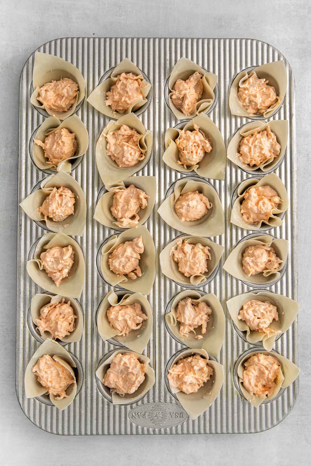 min muffin tin with 24 wonton wrappers filled with buffalo chicken and cheese mixture.