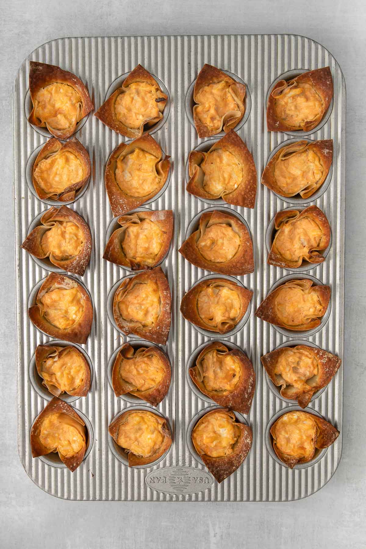 mini muffin tin with 24 wonton wrappers baked with buffalo chicken and cream cheese mixture.