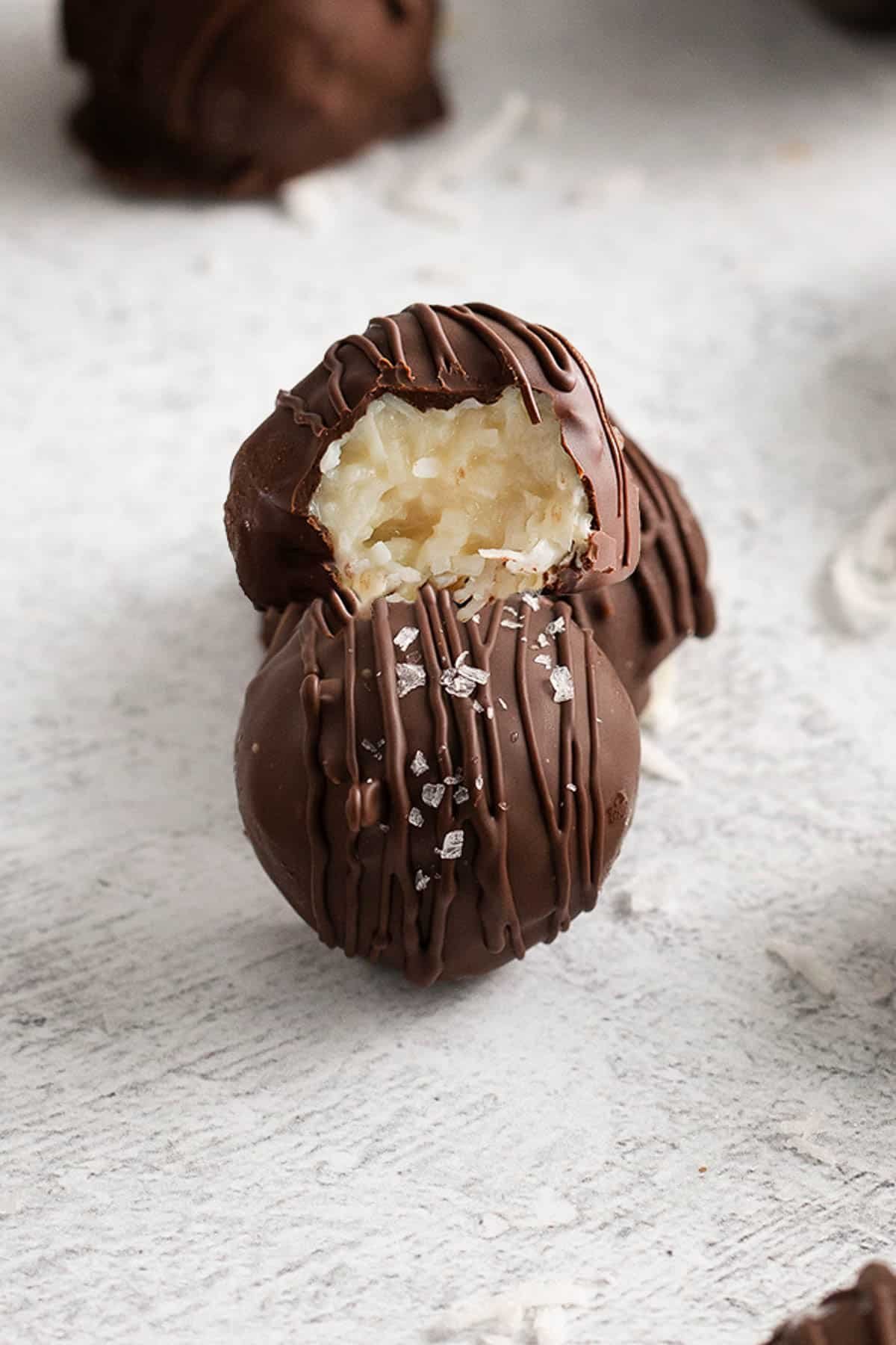 three chocolate coconut truffles with a bite taken out of one.