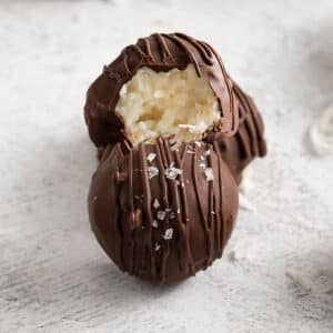 closeup of chocolate covered coconut balls with one with a bite taken out of it.