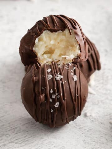 closeup of chocolate covered coconut balls with one with a bite taken out of it.