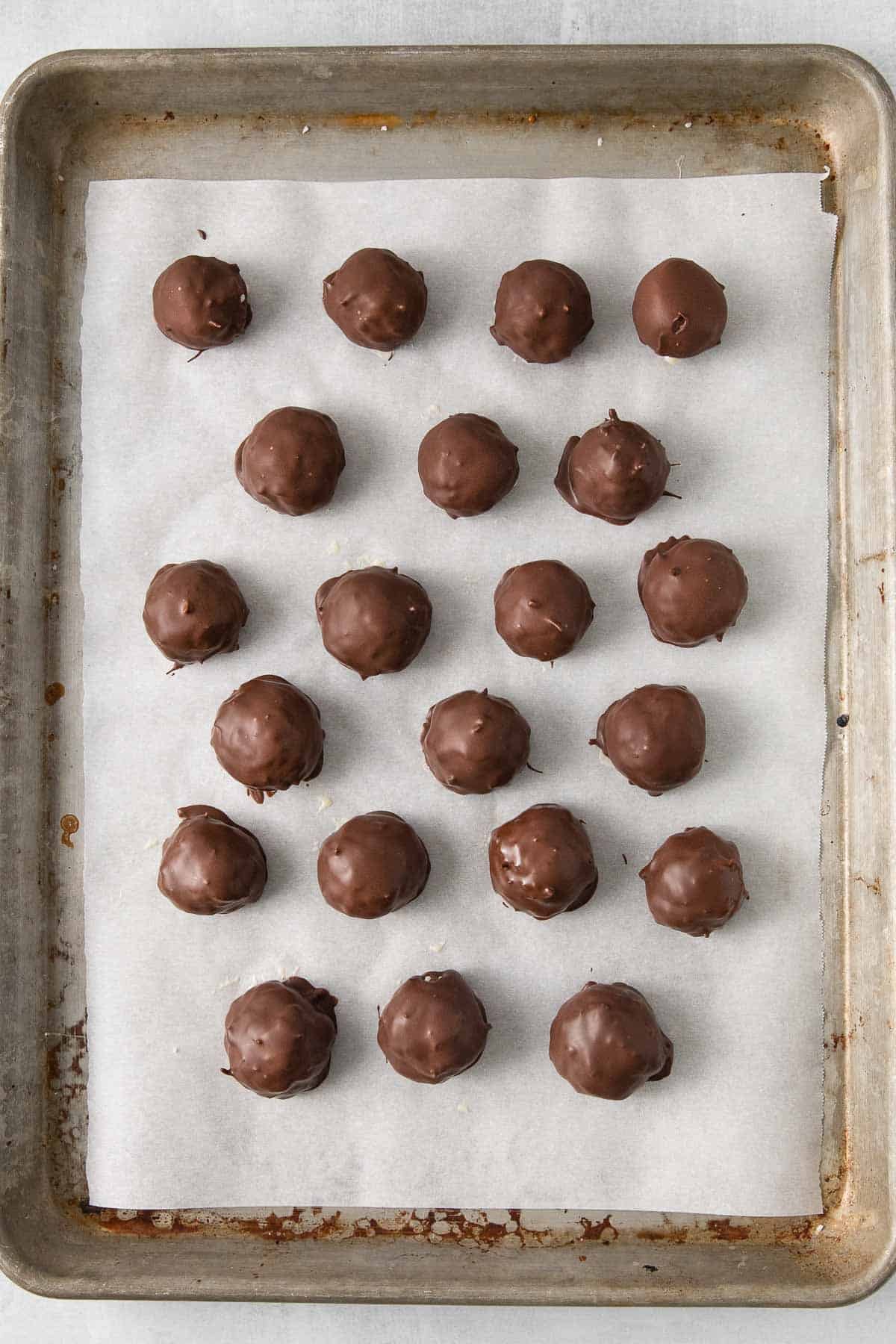 several chocolate coconut balls on a parchment lined baking sheet.
