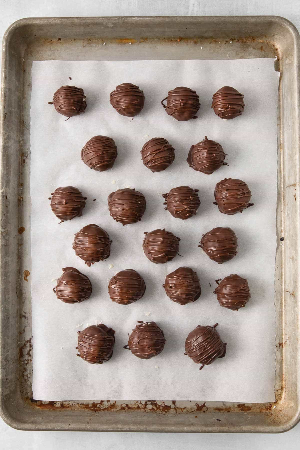 a parchment lined baking sheet with 21 chocolate covered coconut balls drizzled with extra chocolate.
