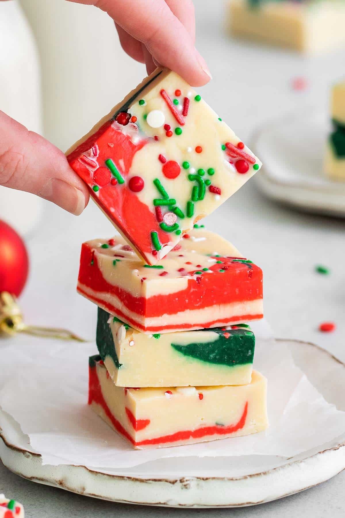 stack of three squares of christmas fudge with a woman's fingers holding a square over the stack.
