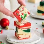 closeup of a red white and green Christmas fudge stacked on a plate with another square being held over top.