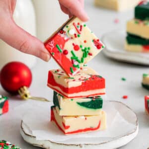 closeup of a red white and green Christmas fudge stacked on a plate with another square being held over top.