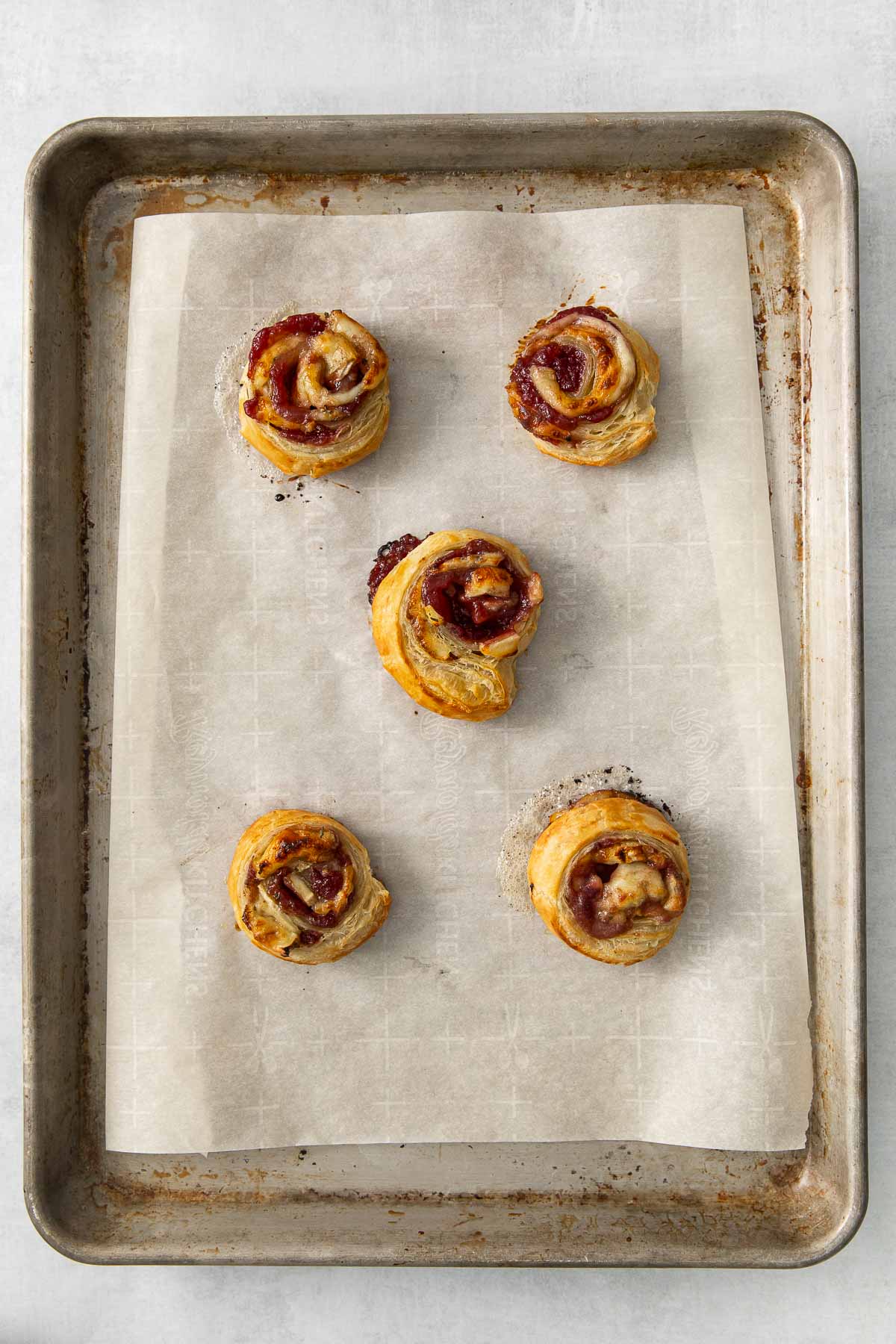 five baked cranberry and brie bites on a parchment lined baking sheet.