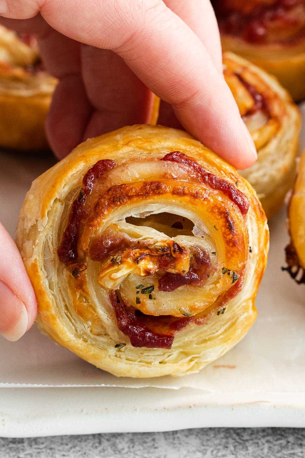 womans fingers holding a puff pastry cranberry brie bite.